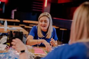 A volunteer wearing a blue fundraising t-shirt happily preparing colourful items and glow sticks for the Wear It Blue fundraiser event, supporting community mental health awareness
