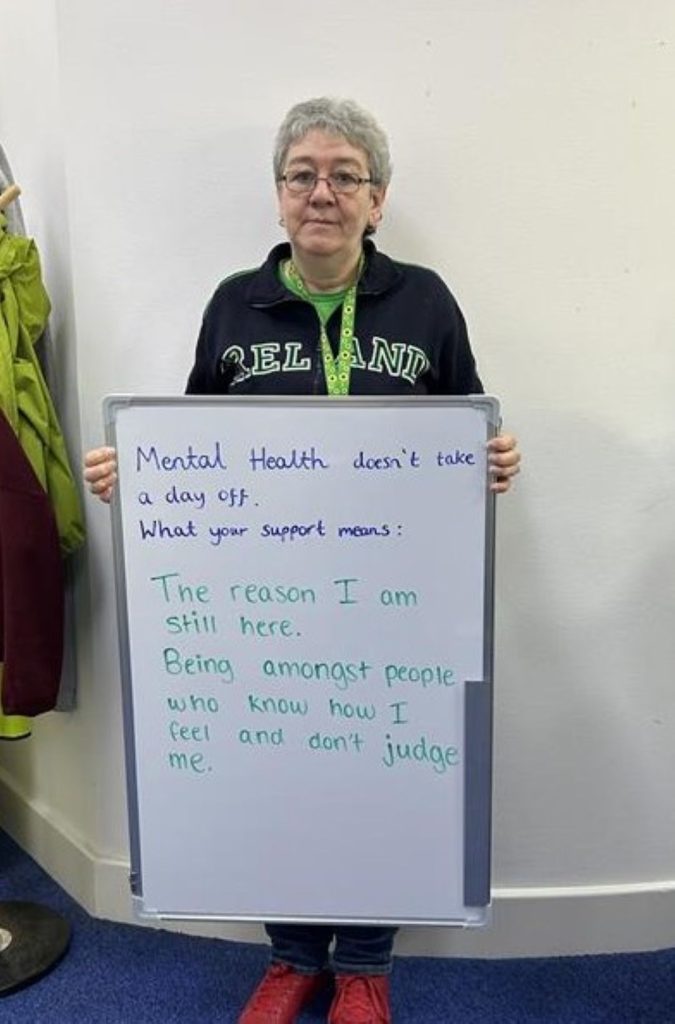 A person wearing a dark green Ireland jumper holds a whiteboard that says: “Mental health doesn’t take a day off. What your support means: The reason I am still here. Being amongst people who know how I feel and don’t judge me.”